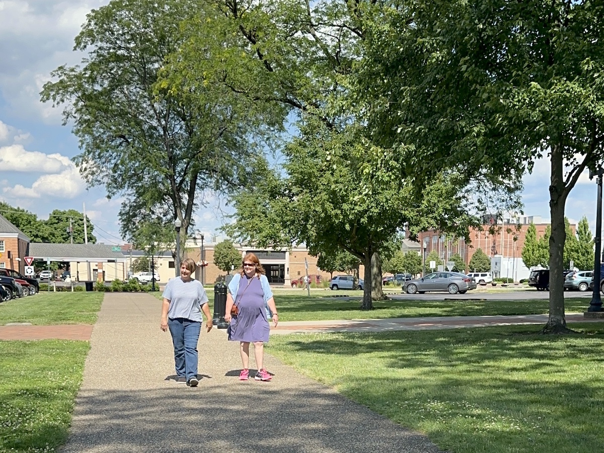 Mary and Lori walking with large green tree in background